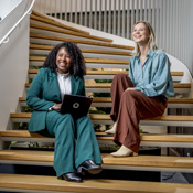 twee vrouwen lachend zittend op trap in werksfeer