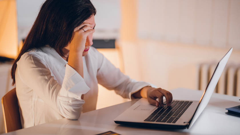 Een vrouw die achter haar bureau zit en naar haar laptop kijkt. De vrouw rust haar hoofd op haar hand en straalt uit teleurgesteld te zijn.