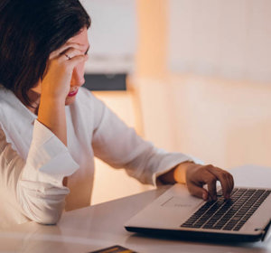 Een vrouw die achter haar bureau zit en naar haar laptop kijkt. De vrouw rust haar hoofd op haar hand en straalt uit teleurgesteld te zijn.