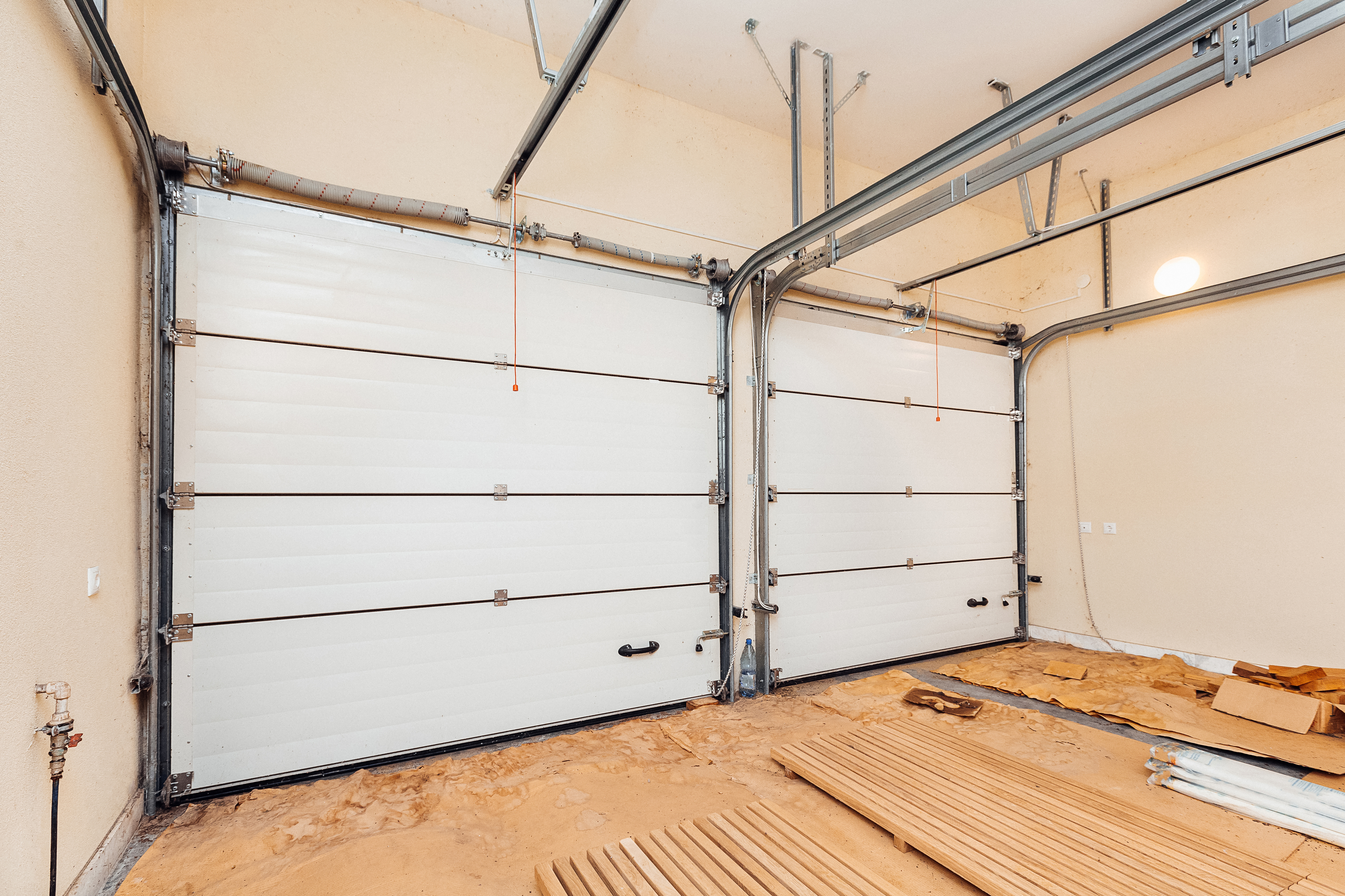 Interieur van een garage met daarin stapels houten planken op een zandige vloer.