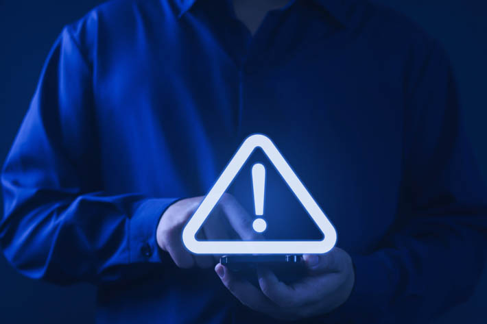 Persoon in donkerblauwe kleding houdt een telefoon vast waarop een lichtgevend waarschuwingsteken met uitroepteken verschijnt.