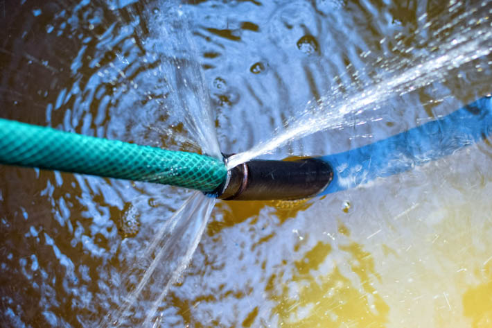 Gebroken tuinslang. Uit het kapotte gedeelte van de tuinslang spuit water.