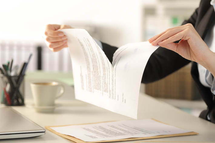 Vrouw zit achter bureau en verscheurt document.