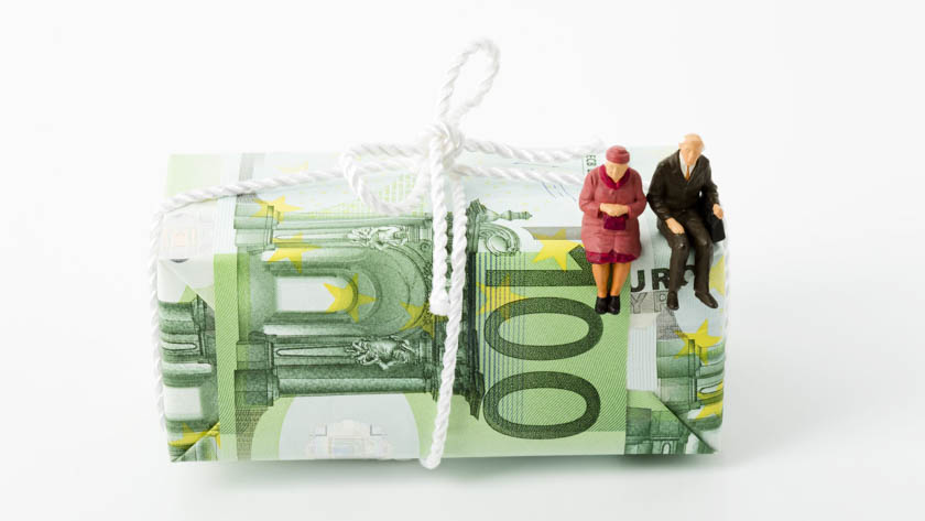 Bundel van 100-eurobiljetten die met een wit touwtje zijn samengebonden. Bovenop de bundel zitten twee kleine figuurtjes van oudere mensen. 