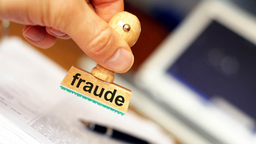 Hand die een stempel met de tekst 'fraude' vasthoudt. De stempel hangt boven enkele documenten.