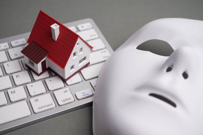 Miniatuurhuis op een computertoetsenbord, naast een wit masker zonder expressie.
