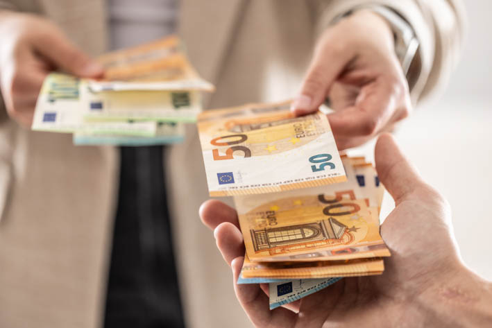 Man overhandigt eurobiljetten aan andere persoon.