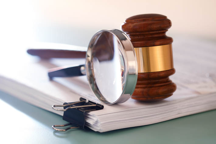 Stapel documenten, met daarop een vergrootglas en een gavel.