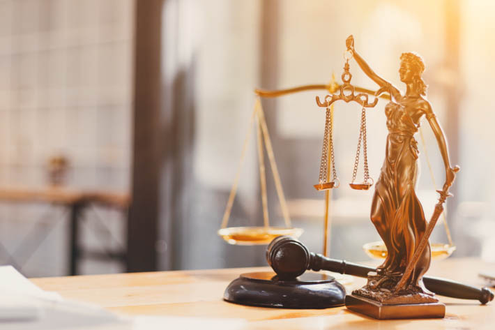 Bronzen standbeeld van Vrouwe Justitia die een weegschaal in de ene hand en een zwaard in de andere hand houdt. Het standbeeld staat op een houten bureau, naast een gavel.