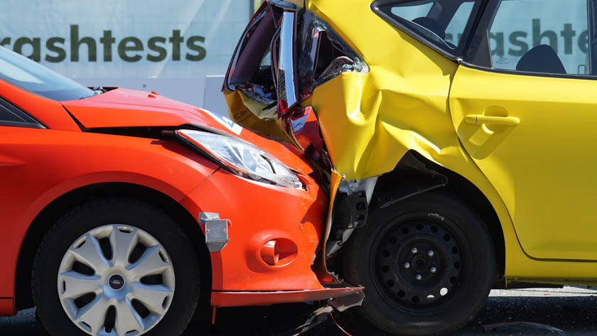 Een crash waarbij een rode auto met aanzienlijke schade aan de voorkant is gebotst op de achterkant van een gele auto, die ook zichtbaar beschadigd is.