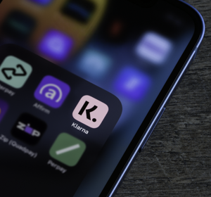 Een close-up van een smartphone waarop een map met betaalapps te zien is, met de Klarna-app duidelijk zichtbaar op het scherm.
