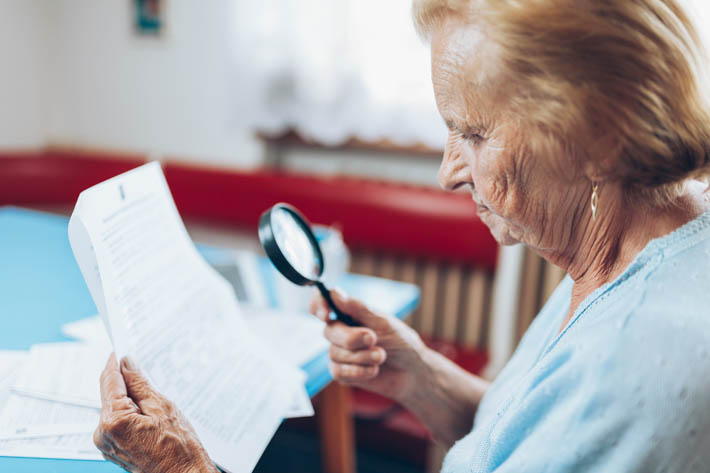 Oudere vrouw leest papieren met vergrootglas.