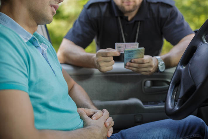 Persoon in een auto en een agent die bij het raam van de automobilist rijdocumenten controleert.