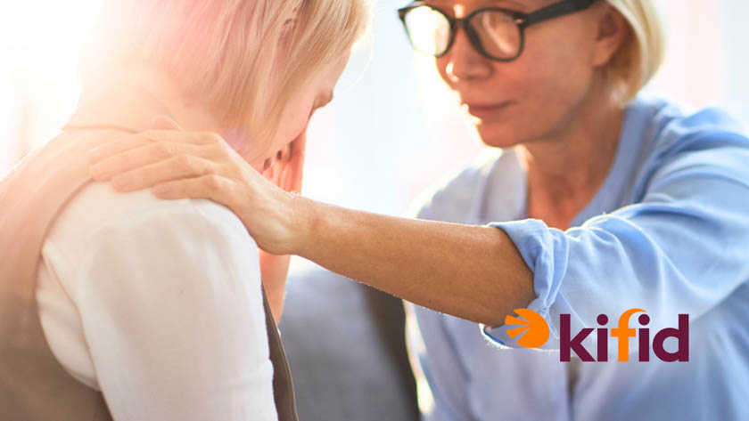 Twee vrouwen die tegenover elkaar zitten. De ene vrouw huilt en de andere vrouw legt haar hand op de schouder van de huilende vrouw en lijkt haar troost te bieden. Rechtsonder is het logo 'Kifid' zichtbaar.