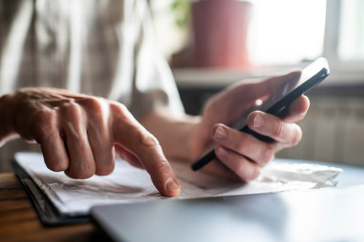 Hand van ouder persoon, die wijst een document. In de andere hand houdt de persoon een telefoon vast.