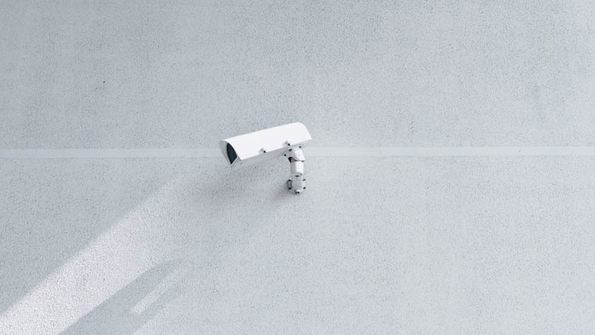 Een witte beveiligingscamera gemonteerd op een lichtgrijze muur.