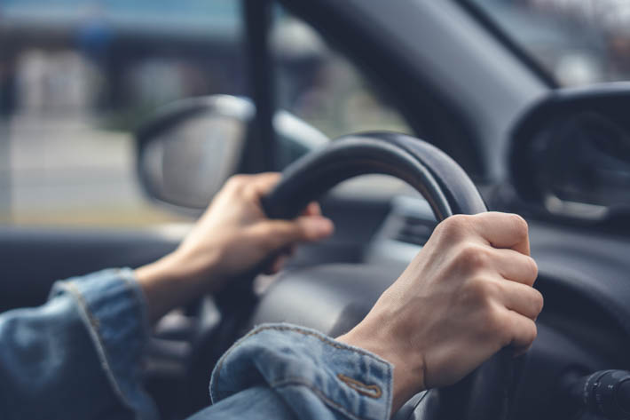 Twee handen die een stuur van een auto vasthouden.
