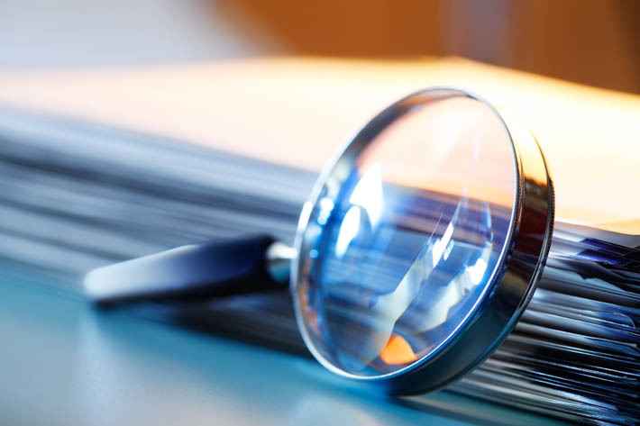 Stapel documenten met vergrootglas.