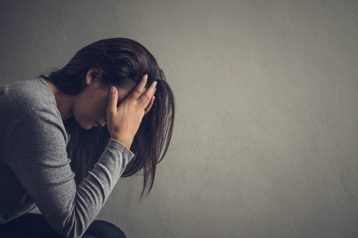 Vrouw zit voorovergebogen met haar handen voor haar gezicht.