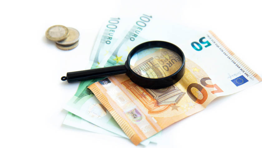 Eurobiljetten, euromunten en een vergrootglas op een witte ondergrond.