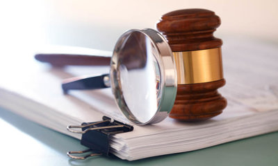 Stapel documenten, met daarop een vergrootglas en een gavel.