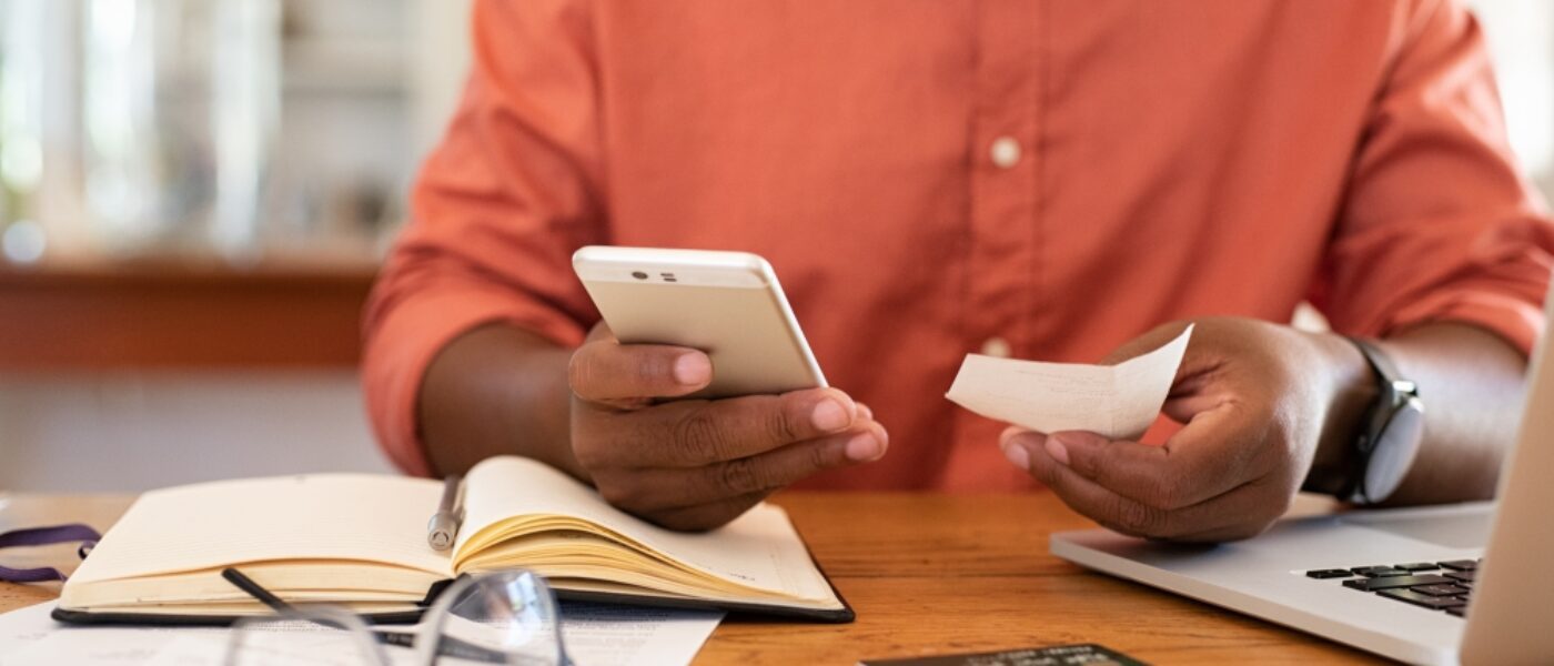 Closeup of man hands using phone to calculate expenses. Man checking invoice balance on mobile phone app. Close up hands of guy taking a closer look at his budget and calculating credit card bills.