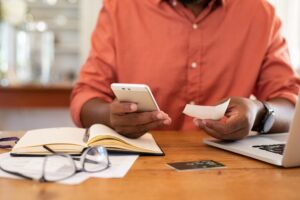 Closeup of man hands using phone to calculate expenses. Man checking invoice balance on mobile phone app. Close up hands of guy taking a closer look at his budget and calculating credit card bills.