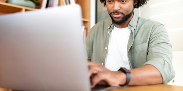 Man in woonkamer zit achter zijn bureau en typt op zijn laptop.